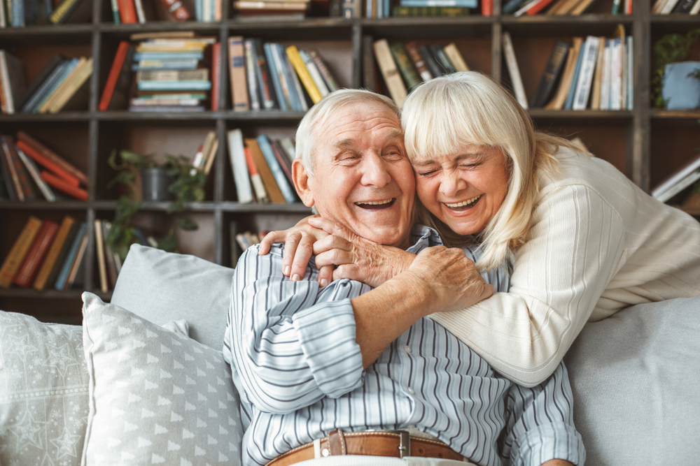 A happy senior couple laughing and embracing on a couch, symbolizing retirement and togetherness.
